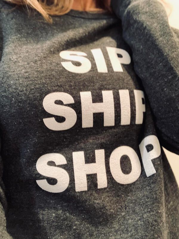 Close-up of a gray sweatshirt with bold white text reading “SIP SHIP SHOP”