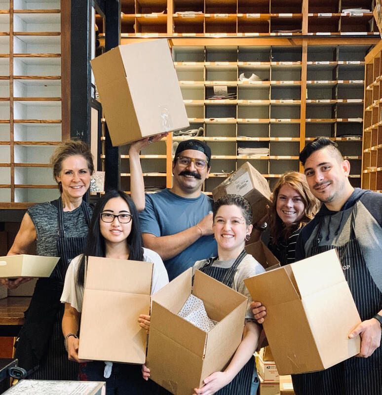 Group of volunteers holding cardboard boxes in a warehouse with shelves in the background