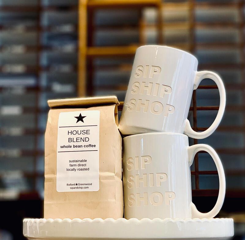 White mugs stacked on a shelf beside a brown House Blend coffee bag in a café display