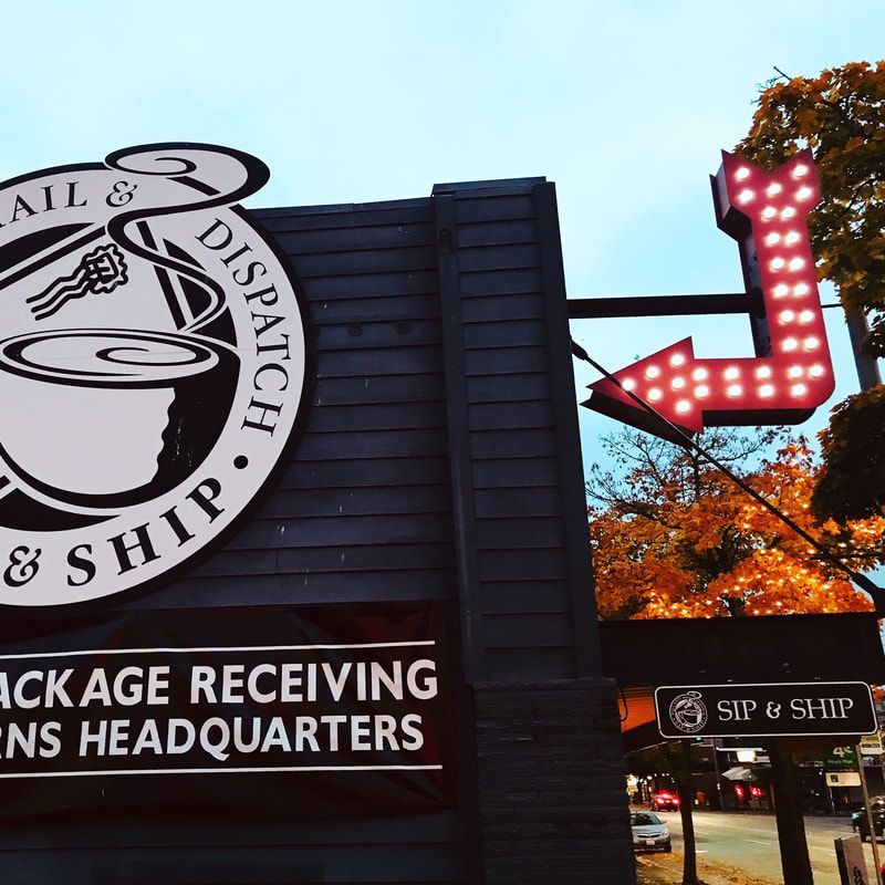Nail & Dispatch package receiving storefront with a red arrow sign at dusk