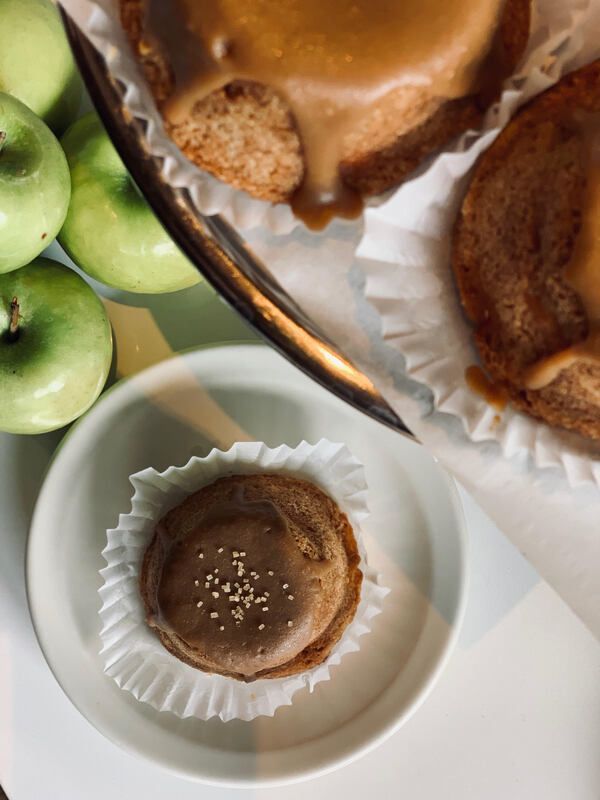 Assorted desserts on a tray with green apples, including caramel-topped cakes and a chocolate tart in a white cup
