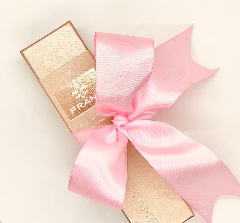 Pink satin ribbon tied around a gold gift box on a pale background