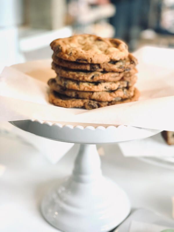Stack of chocolate chip cookies on a white cake stand with a serrated cake server in front