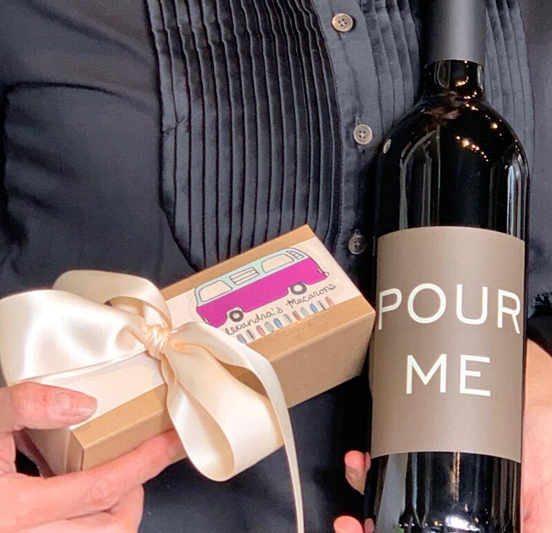 Hands holding a gift box with a ribbon and a black bottle labeled “POUR ME” in a suit pocket view