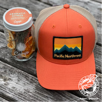 Orange Pacific Northwest cap beside a camp snack jar on weathered wood.