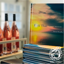 Stack of books with a colorful cover beside rose wine bottles in a bright room