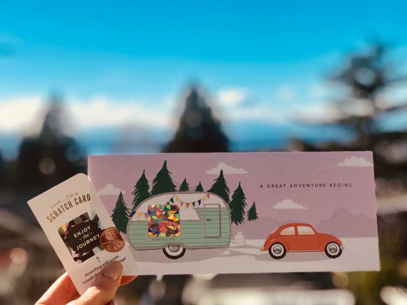 Person holding a ticket book with a retro camper and car illustration against a blurred mountain backdrop