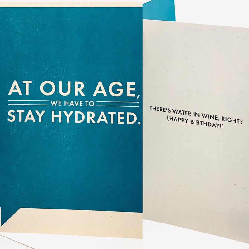 Greeting card with teal and cream panels reading, “At our age, we have to stay hydrated. There’s water in wine, right? (Happy Birthday)”