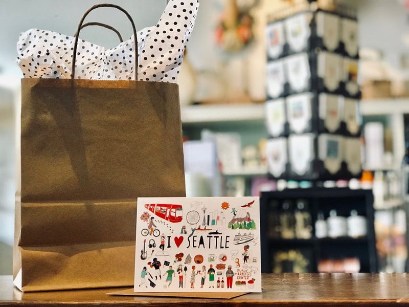 Brown shopping bag and Seattle souvenir card on a store counter, with shelves blurred in the background