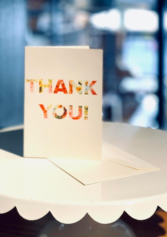 Cream thank-you card standing on a white scalloped cake stand with matching envelope background.