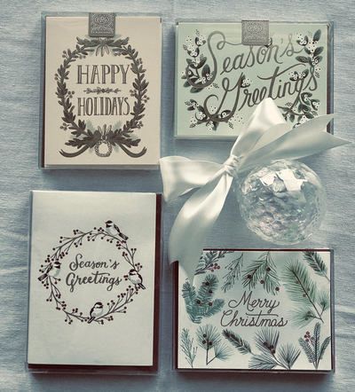 Four holiday greeting cards with festive wreath and pine designs, tied with a white ribbon.