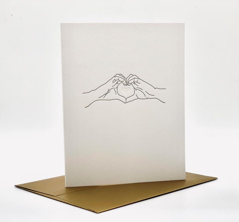 Minimal pop-up card with hands forming a heart above a gold base on a white background
