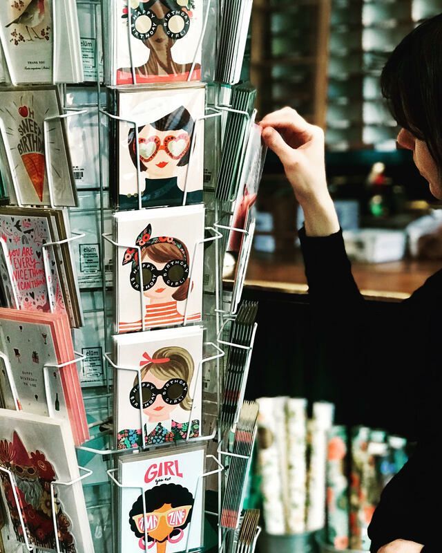 Colorful illustrated cards in a display rack, with a person browsing in the background
