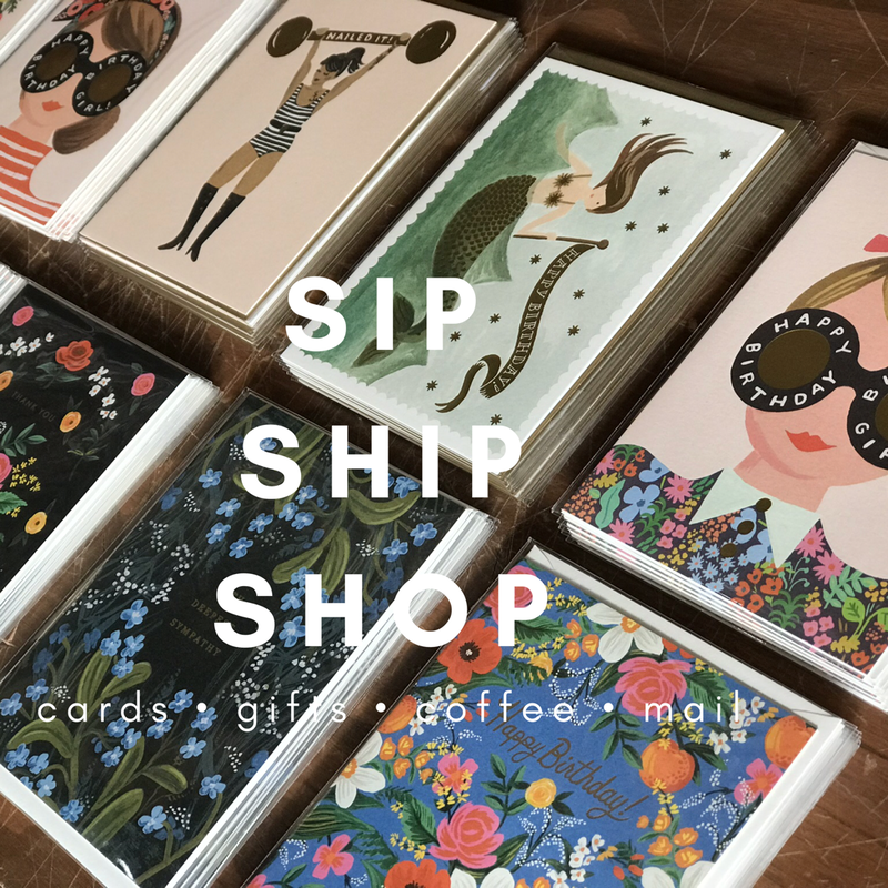 Colorful greeting cards and gifts display reading “SIP SHIP SHOP” in a boutique shop window.