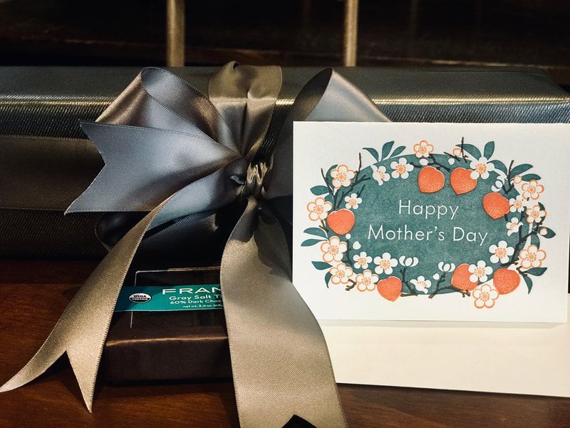 Mother’s Day gift box with a silver ribbon and floral card on a shelf