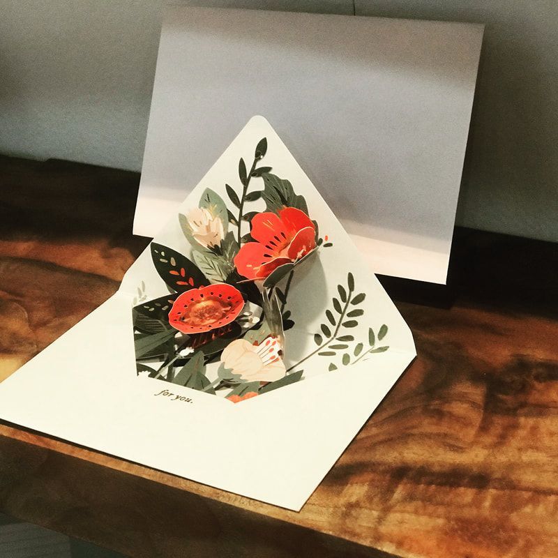 Pop-up greeting card with red and white flowers on a wooden table