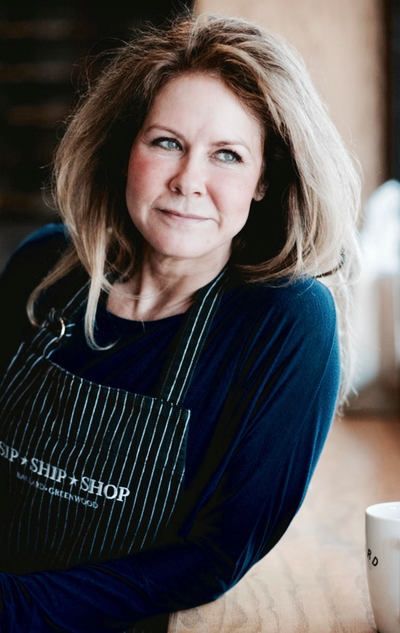 Portrait of a smiling woman in a navy apron in a softly lit café setting