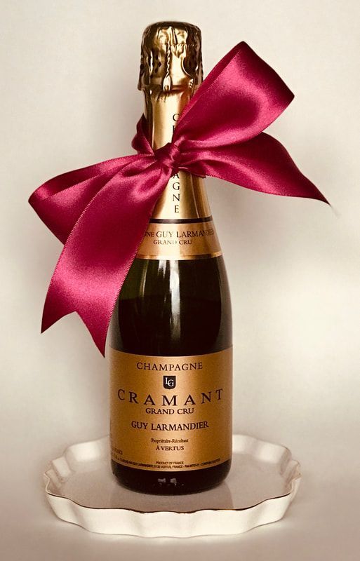 Pink-ribboned champagne bottle on a clear glass stand against a white background