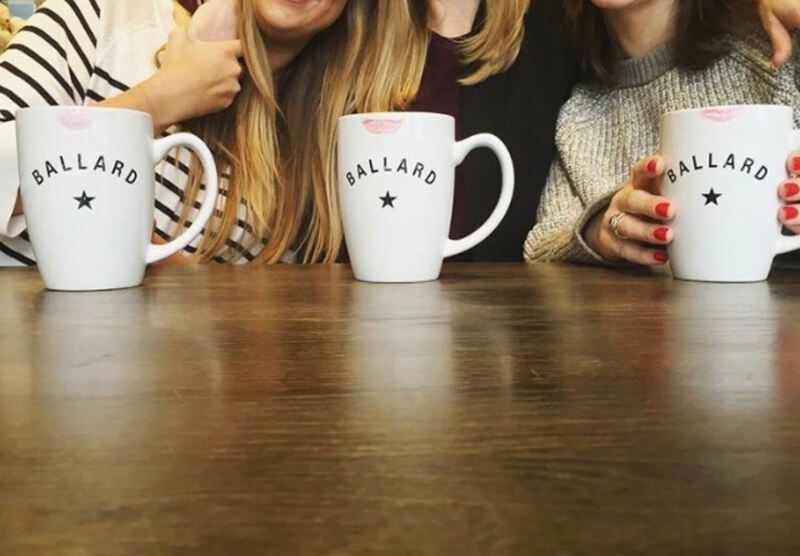 Three people holding white Ballard mugs over a wooden table