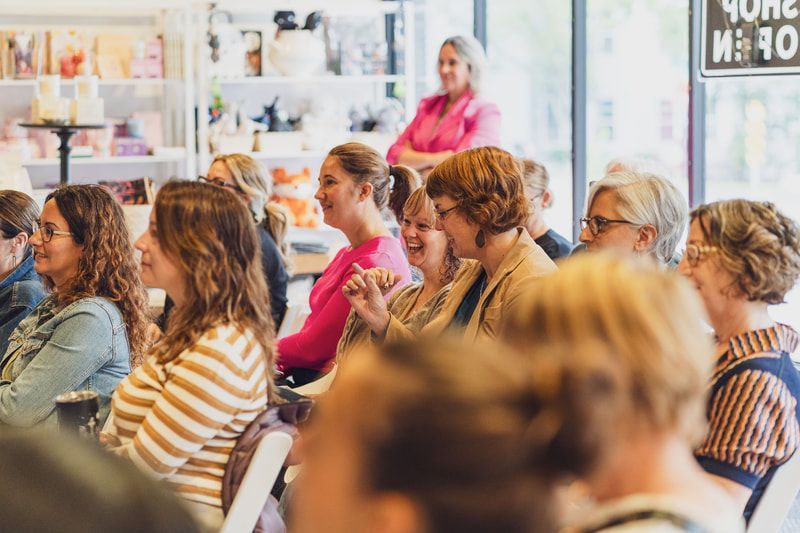 Audience seated in a bright room, listening to a speaker near the back.
