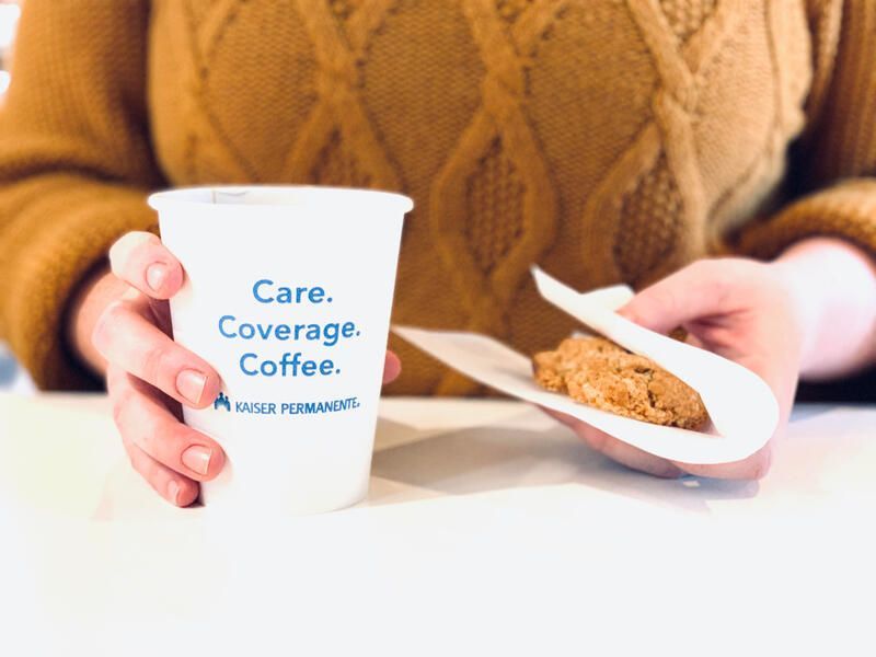 Hand holding a coffee cup beside a plate with a biscotti on a white table.