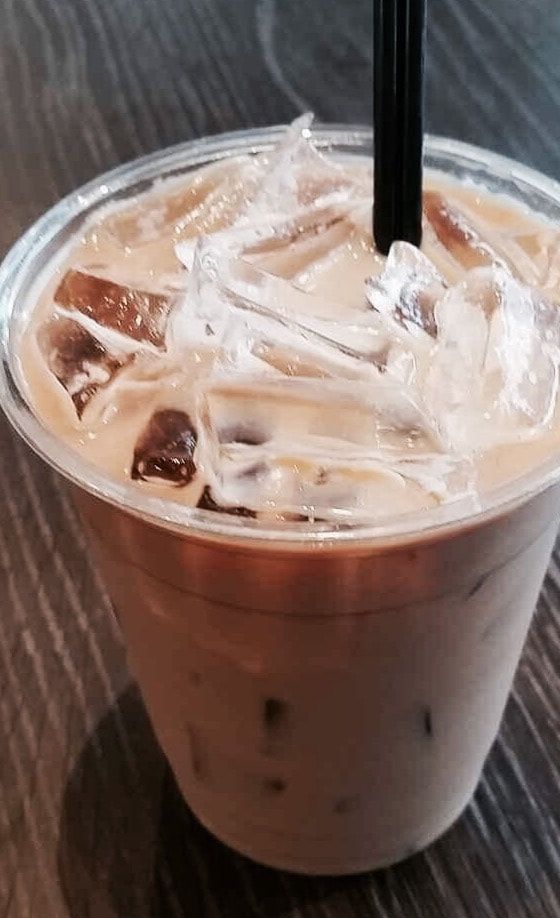 Iced coffee in a clear plastic cup with a black straw and ice, on a table.