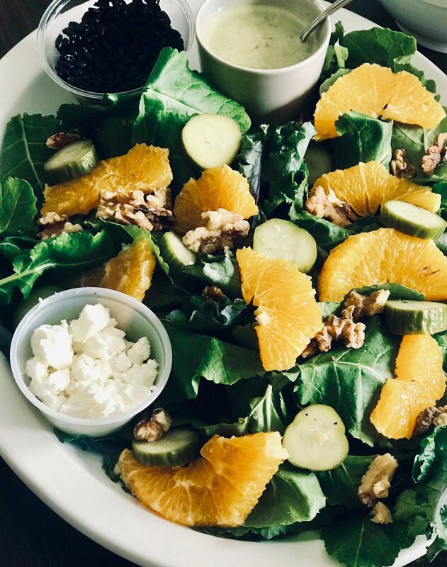 Salad with orange slices, cucumber, greens, walnuts, and bowls of dressing and cheese