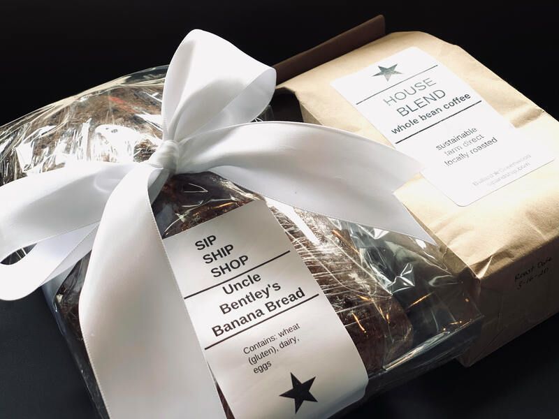 Gift baskets of wrapped baked goods with white ribbon and labels on a dark surface