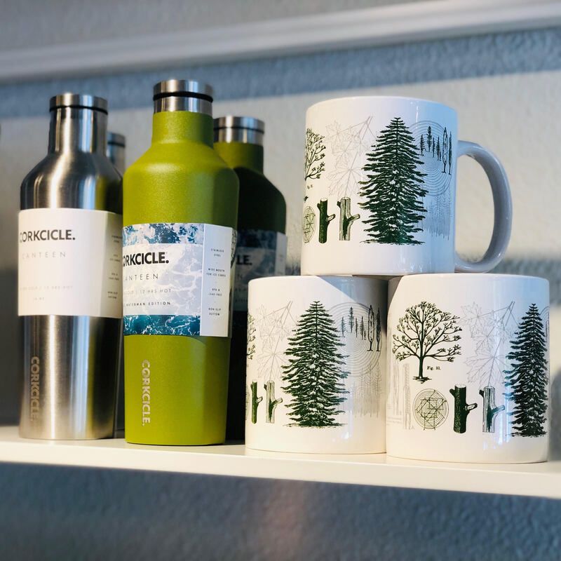Three insulated bottles and three pine tree mugs on a shelf