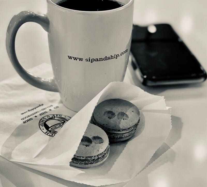 Black-and-white coffee mug beside two macarons on a napkin, with a phone in the background