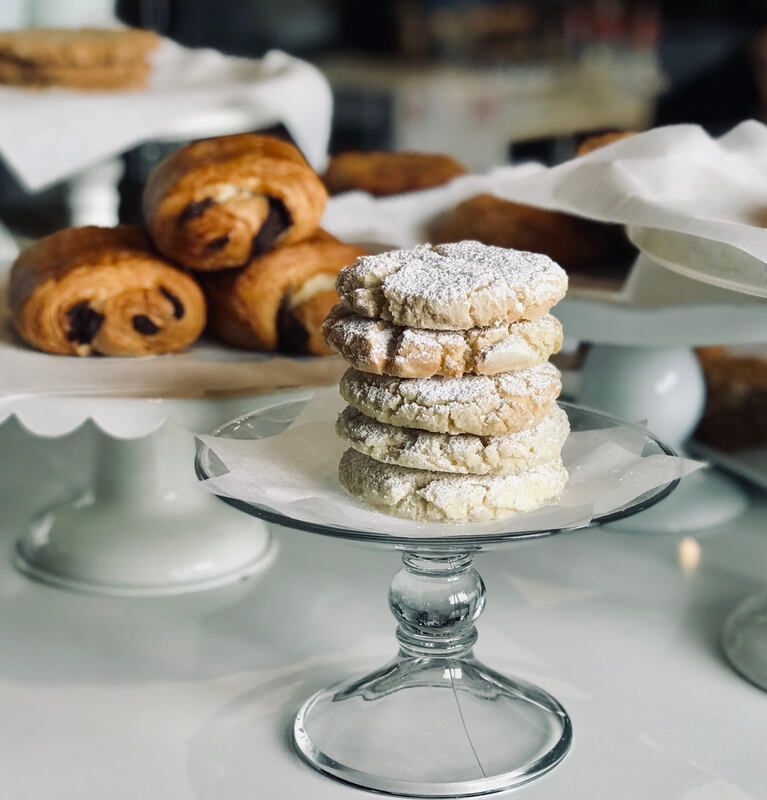 Powdered sugar cookies stacked on glass cake stands beside cinnamon rolls on a dessert table