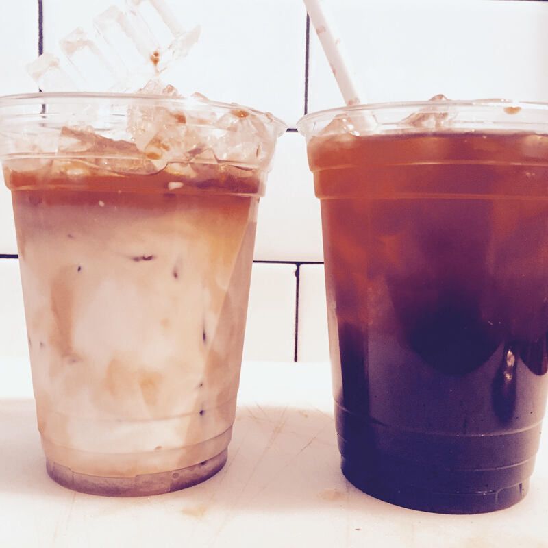 Two iced coffee drinks in clear plastic cups on a table, one light with milk and one dark.