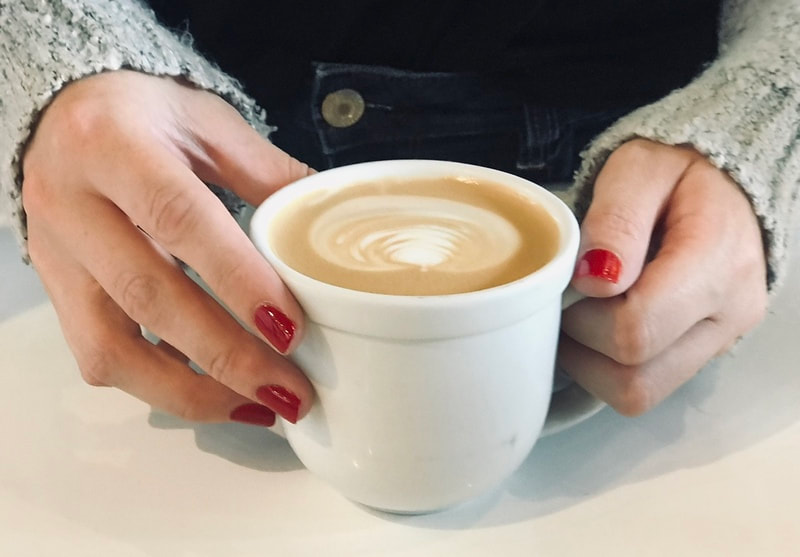 Hands with red nails holding a white cup of latte on a table