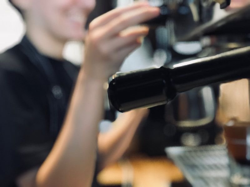 Barista preparing an espresso machine, with a black portafilter in the foreground