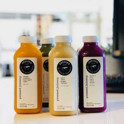 Three bottled juices on a countertop, in orange, pale yellow, and purple with white labels.