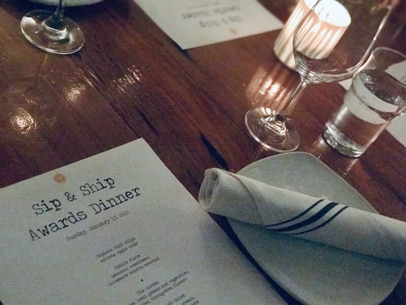 Dinner table setting with menu, folded napkin, water glass, and candlelight on a wooden table