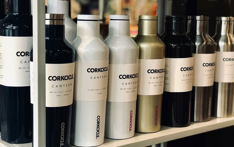 Row of CORGICO-branded stainless steel bottles on a shelf in a store display