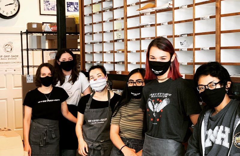 Six masked people standing indoors in front of a wall of shelves and a clock