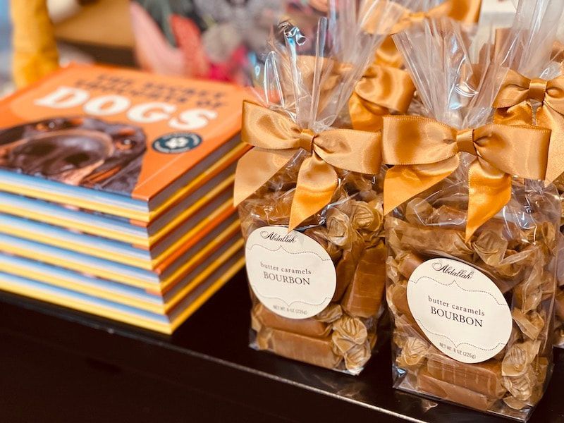 Stack of books beside gift bags of dog treats tied with gold ribbons on a table