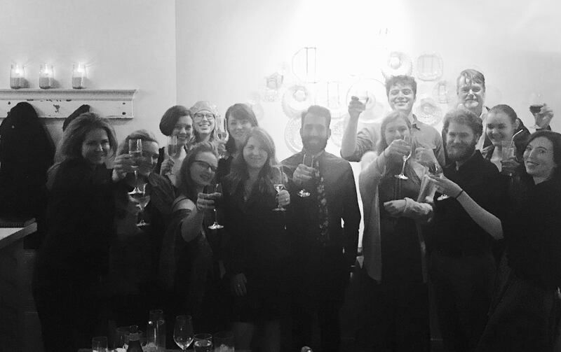 Group of people indoors holding drinks and posing together in a bright room
