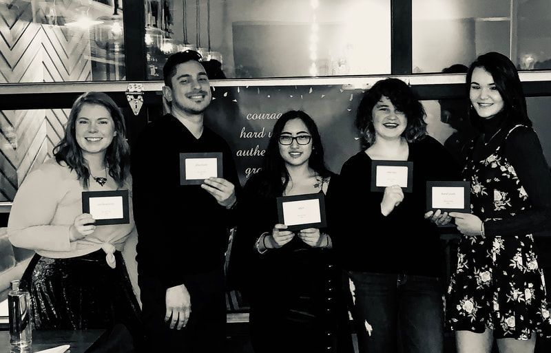Five people holding award plaques and smiling indoors at a celebratory event