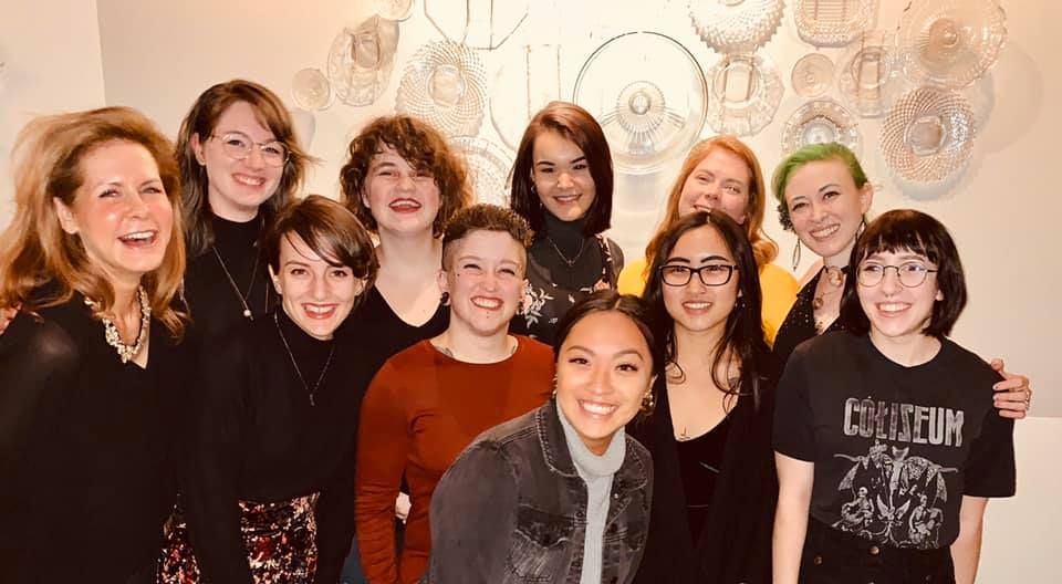 Group of people smiling indoors in front of a decorative wall and lights