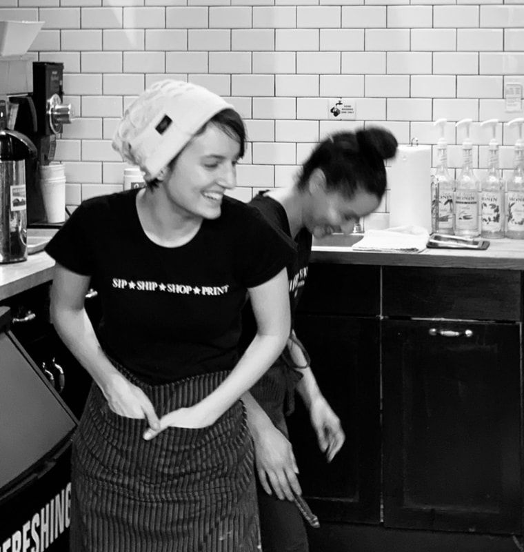 Two people laughing in a tiled kitchen, one wearing a towel on their head and apron.
