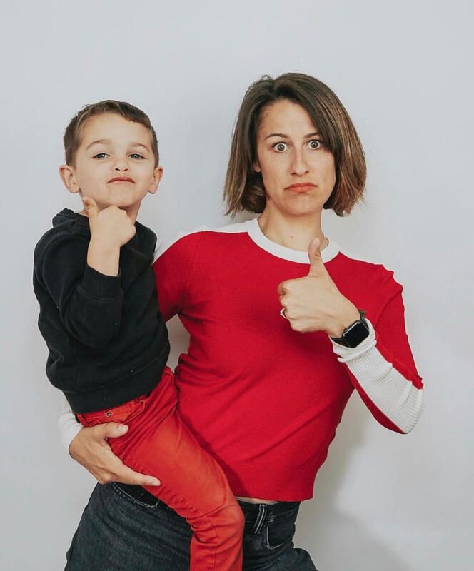 Adult in red shirt holding a child, both giving thumbs up against a plain background