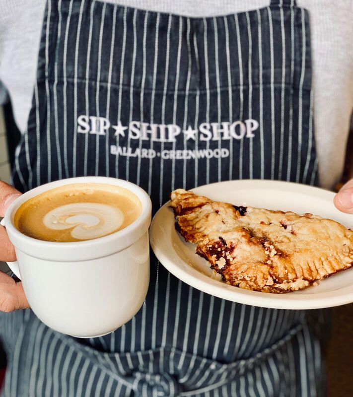 Barista holding a latte and a pastry in front of a striped apron labeled “Sip Shop Shop.”