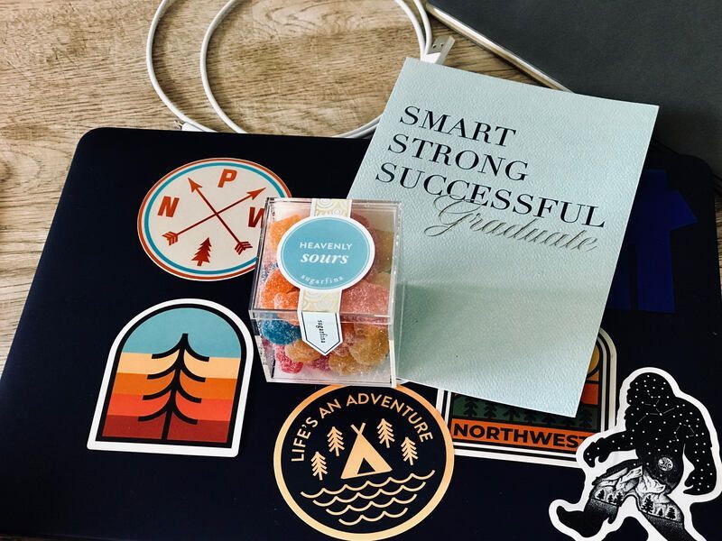 Outdoor-themed stickers and notebook on a wooden surface, including a compass, tent, and “Smart Strong Successful” cover