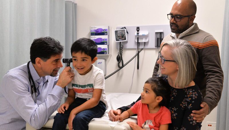 Doctor examining a smiling child in a clinic while family members look on.