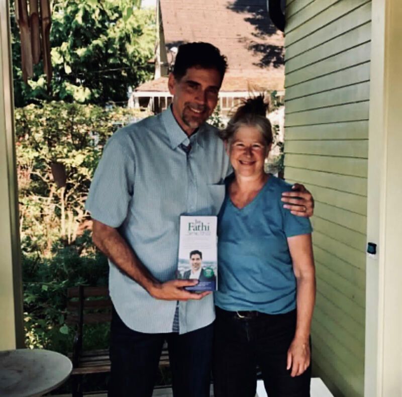Two people smiling on a porch, one holding a book titled “Faith”
