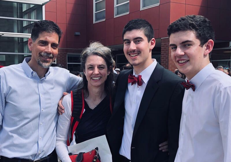Four smiling people posing outdoors in front of a red building, two in formal attire