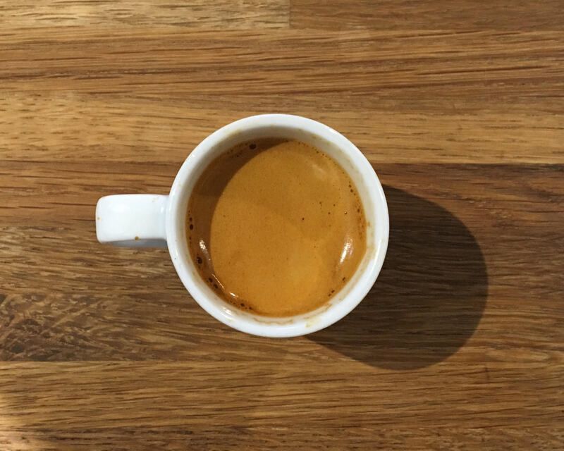 Top-down view of a small white cup of espresso on a wooden table.